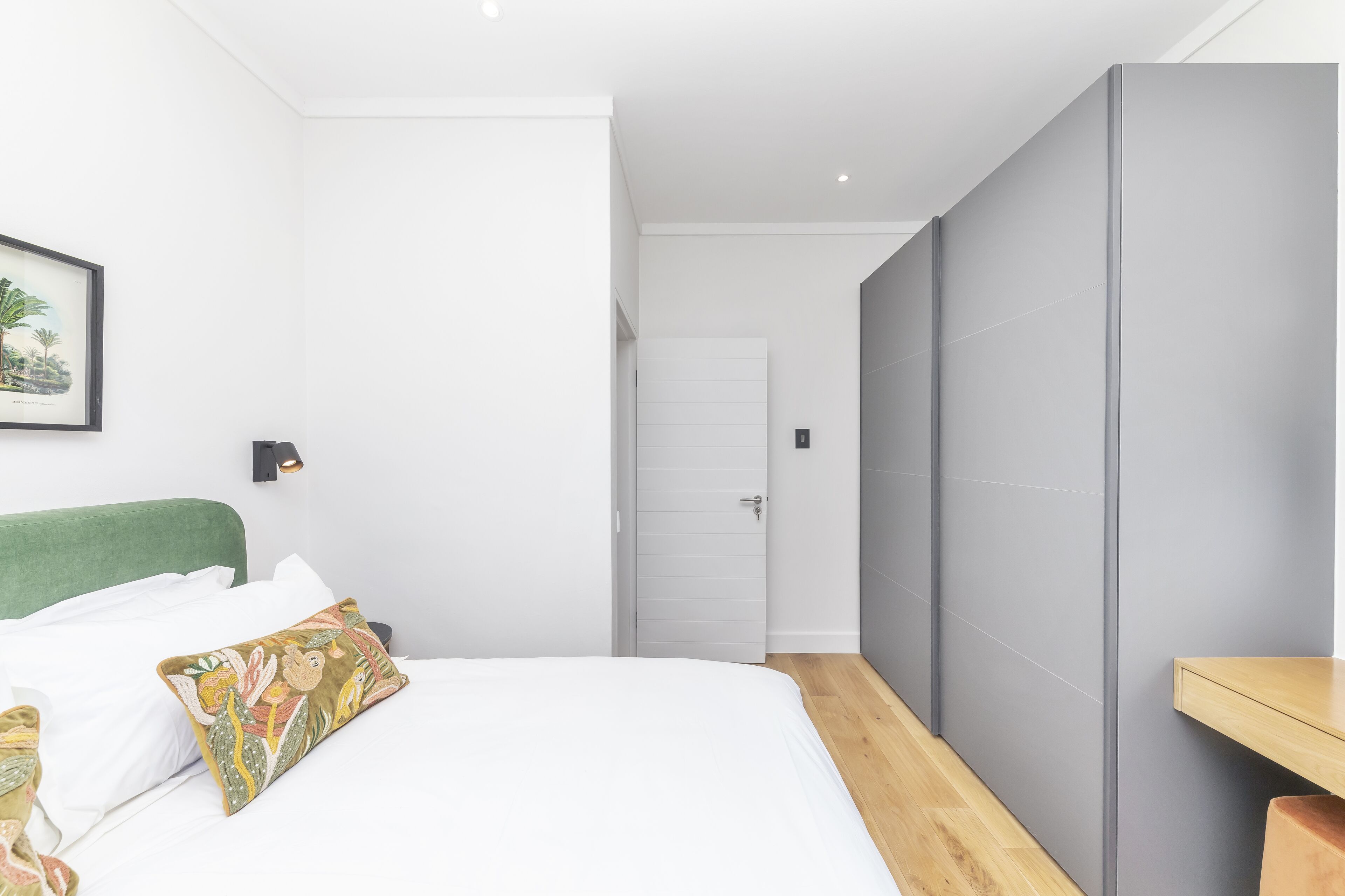 Ein modernes Hotelzimmer mit einem Bett, einem grünen Kopfteil, einem Nachttisch aus Holz und einer grauen Raumtrennwand.
