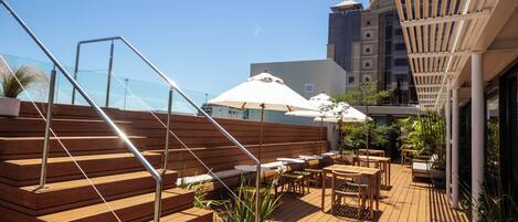 Una terraza de madera con asientos exteriores, una escalera y una barandilla de cristal.