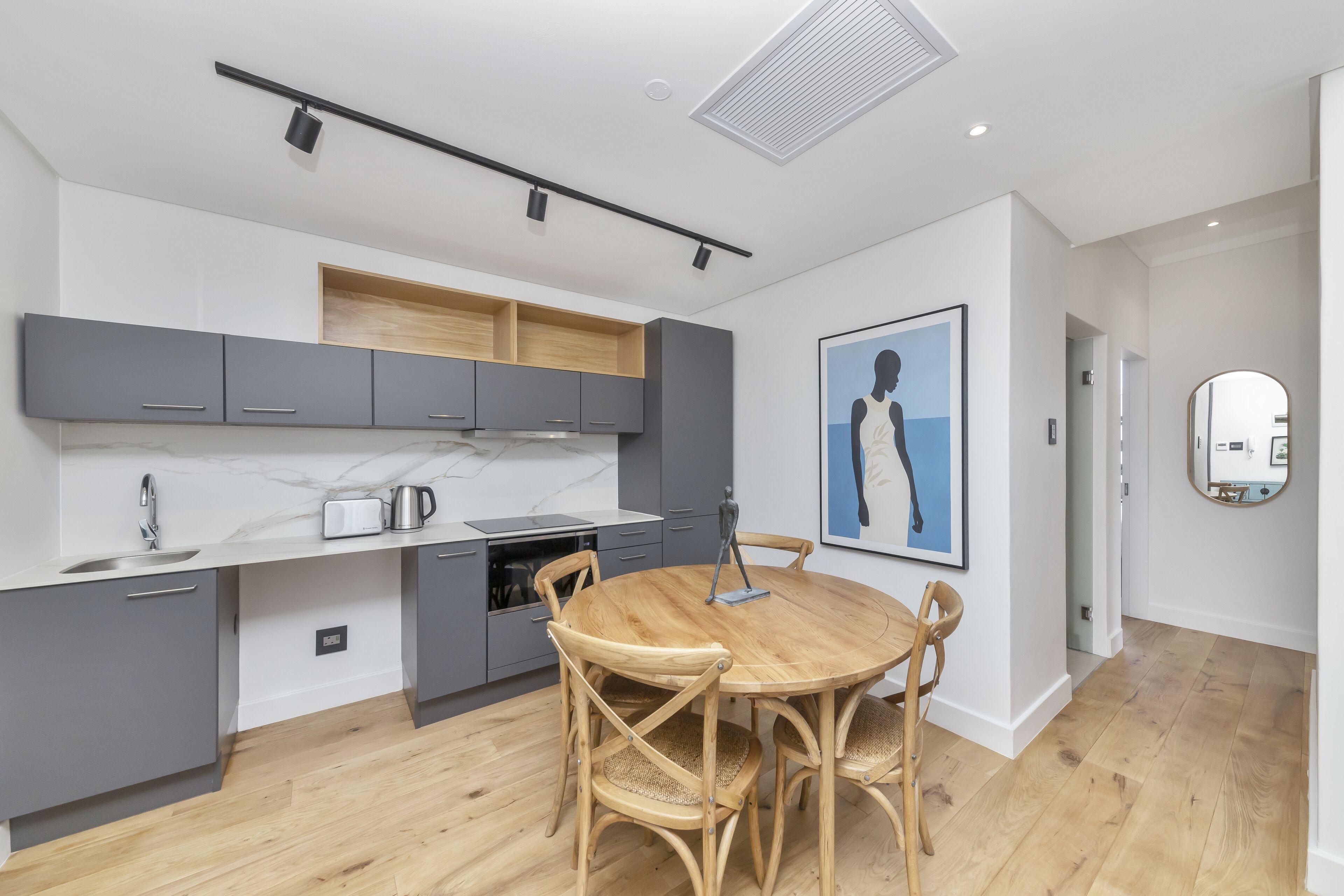Una cocina moderna con armarios grises, una mesa de comedor de madera y una obra de arte grande enmarcada en la pared.