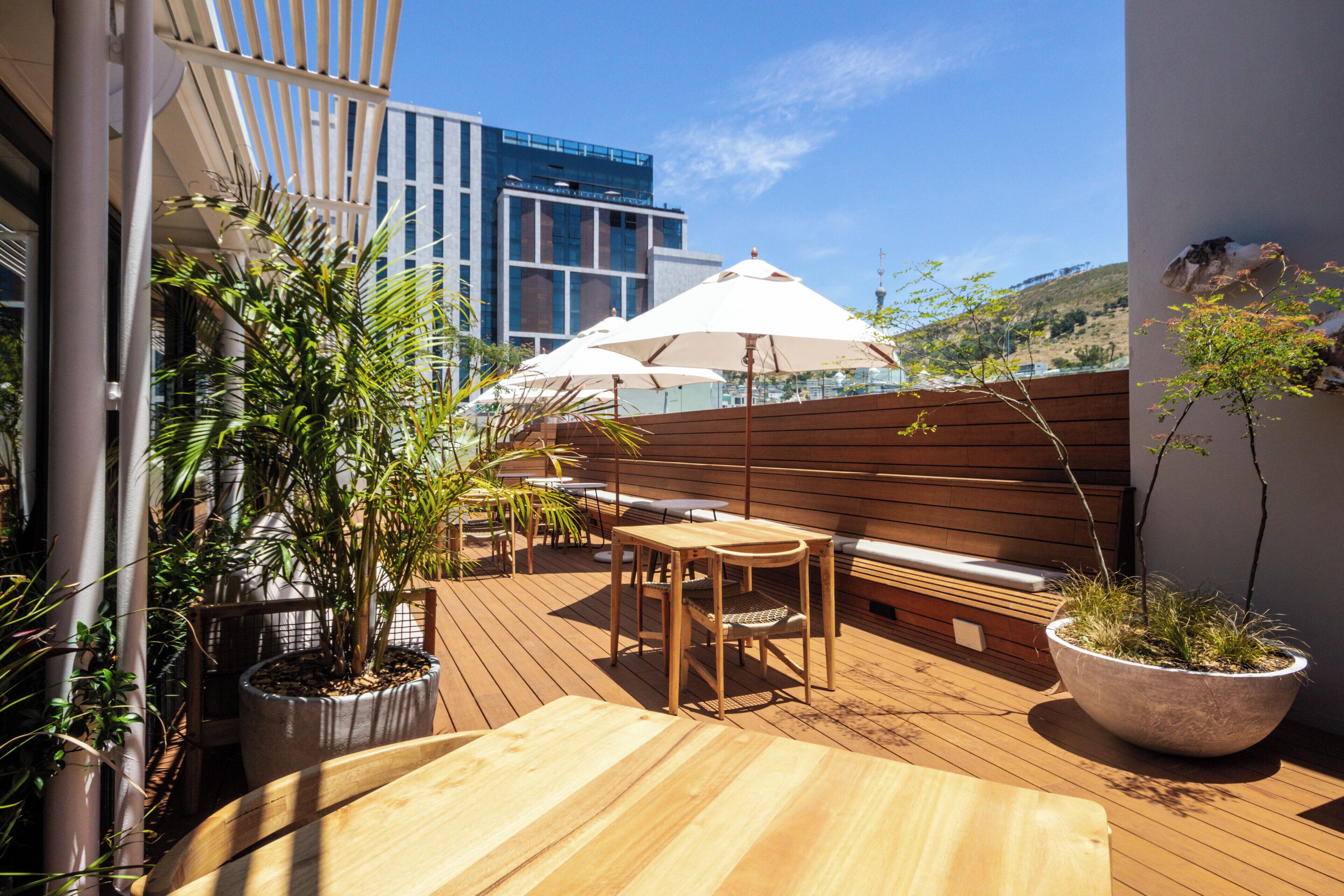 A wooden deck with outdoor seating, potted plants, and a view of a modern building.