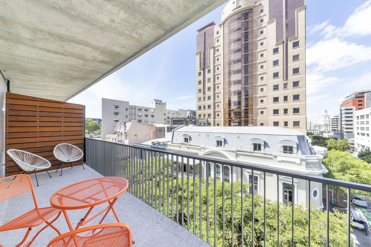 A balcony with orange metal chairs and a wooden slatted wall.