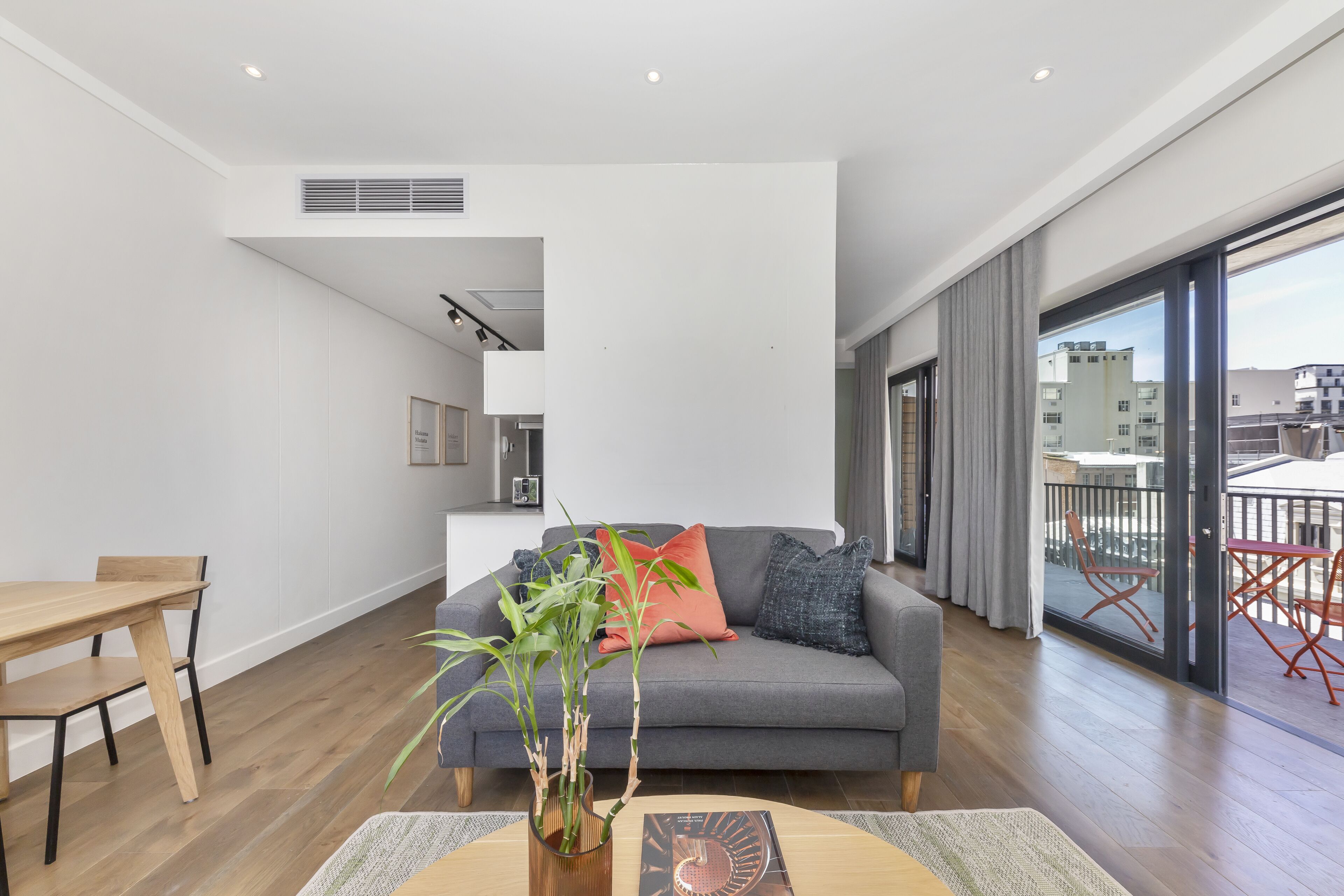 A modern living room with a grey sofa, wooden dining table, and a large window with a view of buildings.