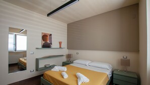 Ein modernes Hotelzimmer mit einem großen Bett, einem Nachttisch, einem Spiegel und einem Fenster mit Jalousien.