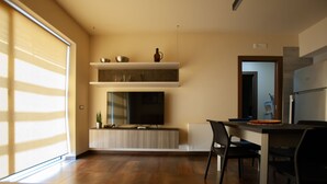 Ein modernes Wohnzimmer mit Flachbildfernseher, Holzboden und einem Essbereich mit Stühlen und Tisch.