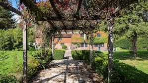 Uma passagem de pedra leva a um edifício de tijolos com um jardim e um pérgola.