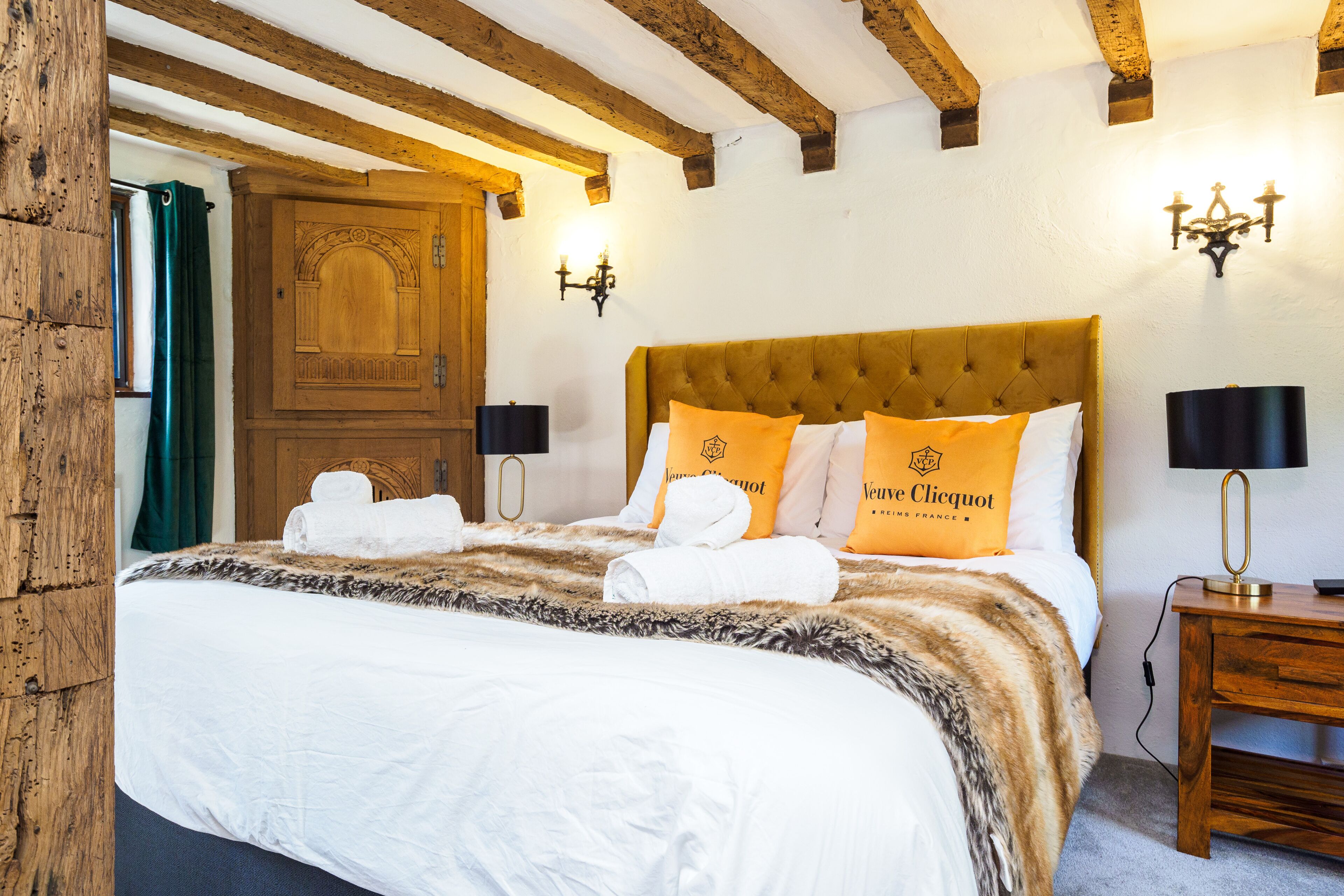 Een hotelkamer met een groot bed, houten balken in het plafond, een houten deur en twee wandlampen.