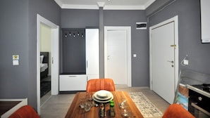 A dining area with a wooden table set for four, a grey wall, and a door leading to a bedroom. - Arpaçay Apart Otel (Arpaçay)
