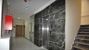 A hallway with a marble wall, a red object on the left, and a staircase on the right. - Arpaçay Apart Otel (Arpaçay)