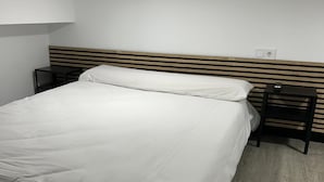 Ein ordentlich bezogenes Bett mit weißen Laken in einem schlichten Zimmer, ausgestattet mit einem Holzkopfstück und zwei Nachttischen.