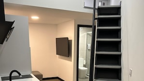 Eine moderne Küche mit einem schwarzen Spülbecken, einem flachbildfernseher an der Wand und einer Treppe zu einem Badezimmer.