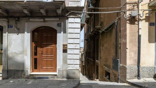 Une vue de rue avec une porte en bois, un mur de pierre et un bâtiment doté d’un balcon.