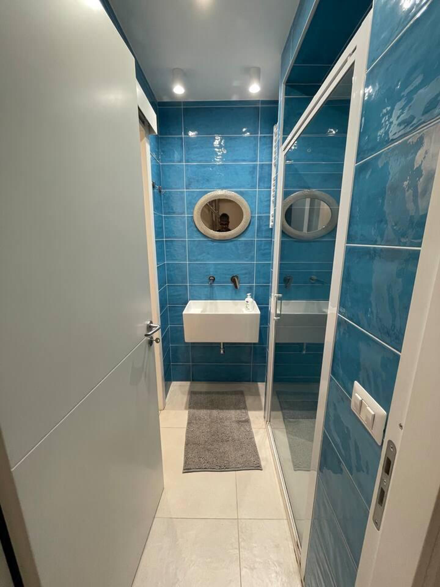 Un baño con lavamanos blanco, espejo y paredes con azulejos azules.