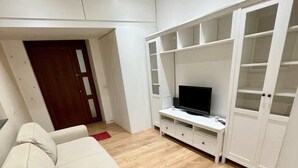 Un salon avec un canapé blanc, un téléviseur posé sur un meuble blanc et un plancher en bois.