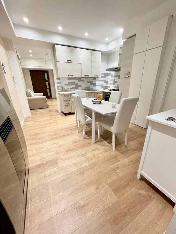 A modern kitchen with white cabinetry, a dining table with chairs, and a light wood floor.