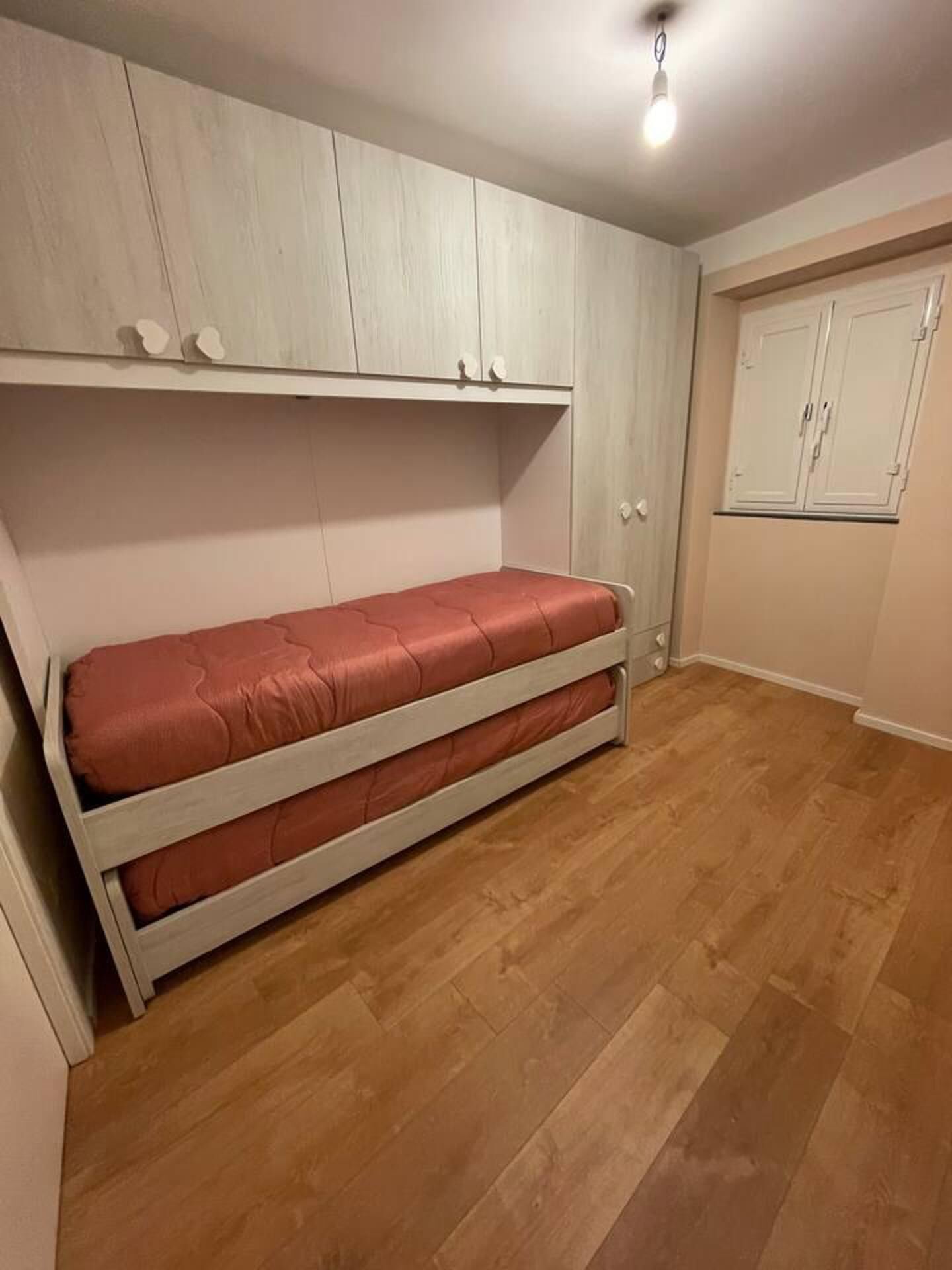 A compact room with a built-in bed, wooden flooring, and a wardrobe with a mirror.