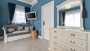 A room with a blue wall, a white sofa with patterned cushions, a white dresser with drawers, a flat-screen TV mounted above the sofa, and a wicker basket on the floor. - Luxurious home in Vucetinec (Vucetinec)