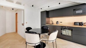 A modern kitchen with a black countertop, white chairs, and a built-in oven. - A Refined 1-BR appartment in Saint-Germain (Paris)