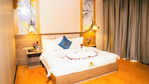 A hotel room with a wooden bed, white linens, a blue pillow, decorative pillows, a bedside table with a vase of flowers, and a wall with a marble-like design. - Sunshine Hotel (Phnom Penh)