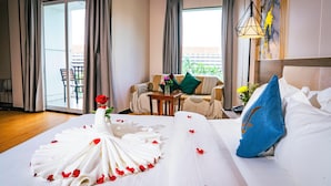 A hotel room with a large bed, a sofa, a table with a vase of flowers, and a view of the outside. - Sunshine Hotel (Phnom Penh)