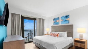 Une chambre d’hôtel comprenant un lit, deux lampes de chevet, un téléviseur fixé au mur, un bureau et un balcon avec une chaise.