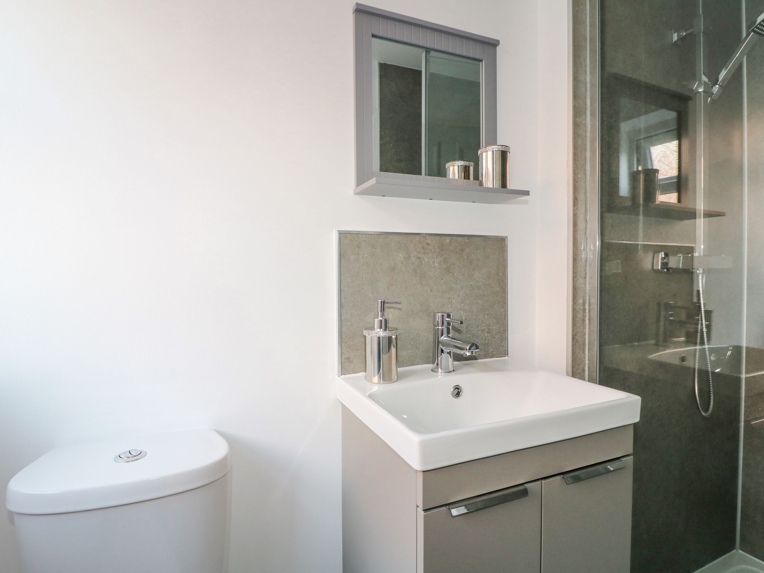 A modern bathroom with a white sink, a toilet, and a glass-enclosed shower area.