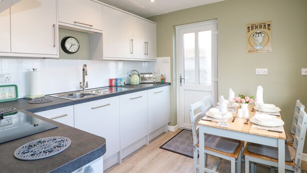 Una cocina moderna con armarios blancos, un lavamanos, un hervidor y un comedor con una mesa preparada para cuatro personas.