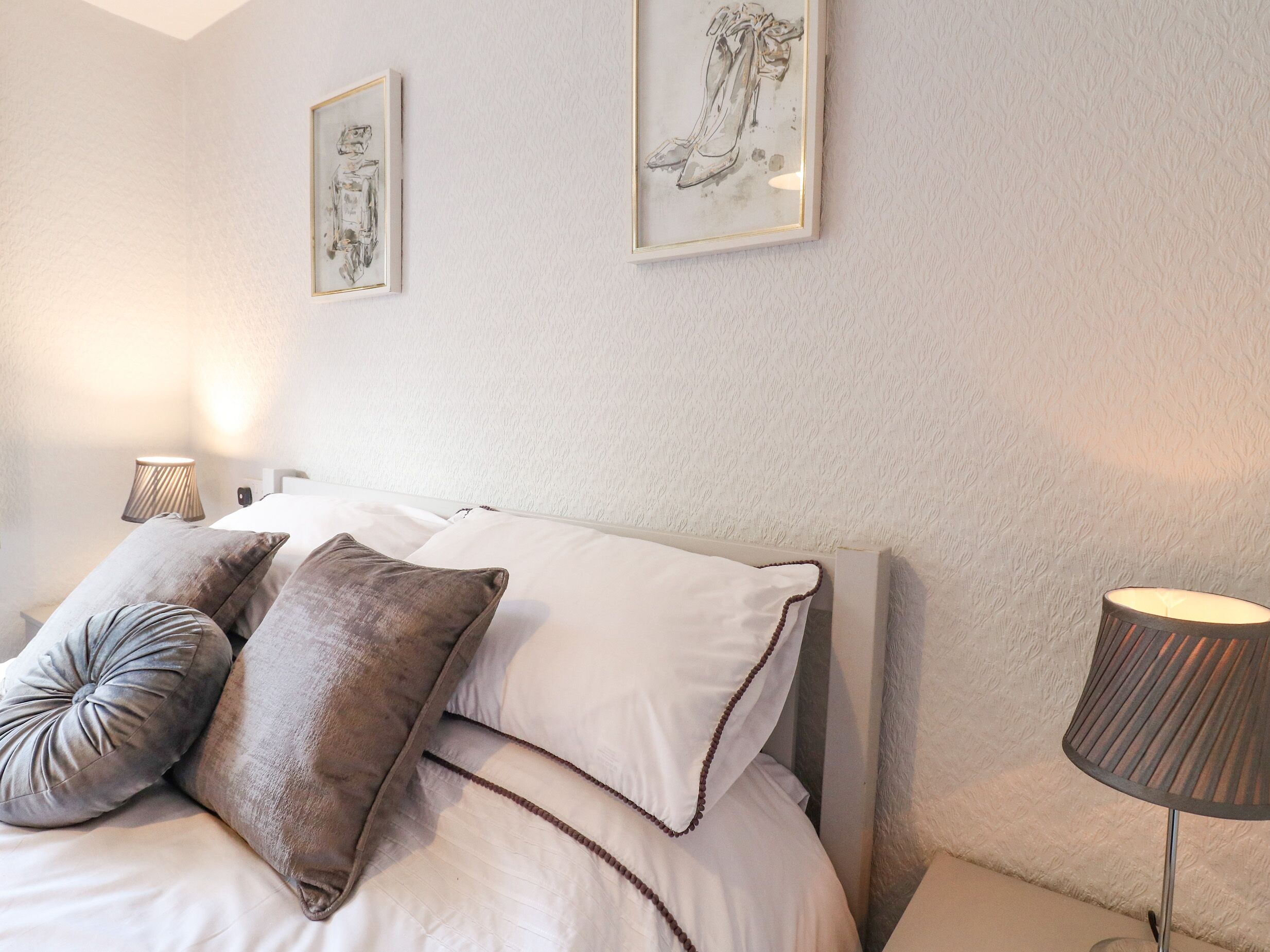 A neatly made bed with two pillows, a bedside lamp, and two framed artworks on the wall.