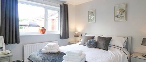 A neatly arranged bedroom with a bed, bedside tables, a window with curtains, and wall art.