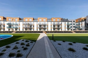 A modern apartment building with multiple balconies, a swimming pool, and a landscaped garden area. - Stylish Apartment with Balcony | Close to the Beach | Parking (Międzyzdroje)