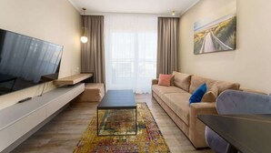 A modern living room with a flat-screen TV, a sofa, a coffee table, and a painting on the wall.