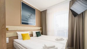 A hotel room with a large bed, a headboard, a framed artwork, and a window with curtains.