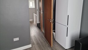 A narrow hallway with a white refrigerator, a wooden door, and a white radiator. - Impeccable 3-bed Apartment in Bradford to Explore (Bradford)
