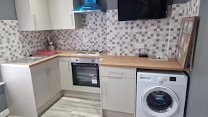 A compact kitchen with white cabinets, a built-in oven, a washing machine, and a flat-screen TV mounted on the wall. - Impeccable 3-bed Apartment in Bradford to Explore (Bradford)