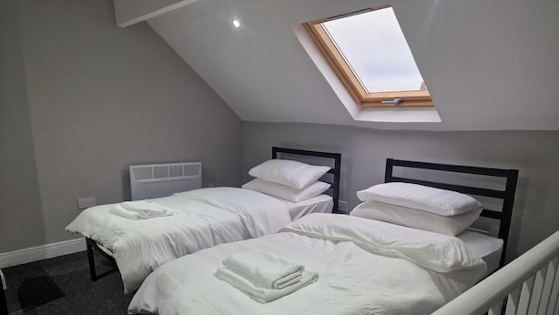 A bedroom with two beds, a skylight, a radiator, and a white crib. - Impeccable 3-bed Apartment in Bradford to Explore (Bradford)