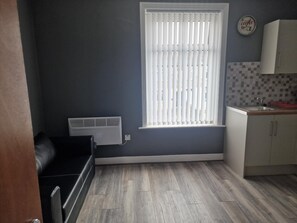 Een kleine keuken met een raam, witte kastjes en een betegelde achterwand.