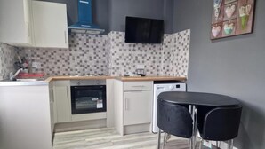 A compact kitchen with a microwave, oven, and dishwasher. There is a small dining area with two chairs and a table. - Impeccable 3-bed Apartment in Bradford to Explore (Bradford)