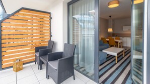 A modern living area with a balcony, wicker furniture, a glass door leading to a kitchen, and a striped rug.