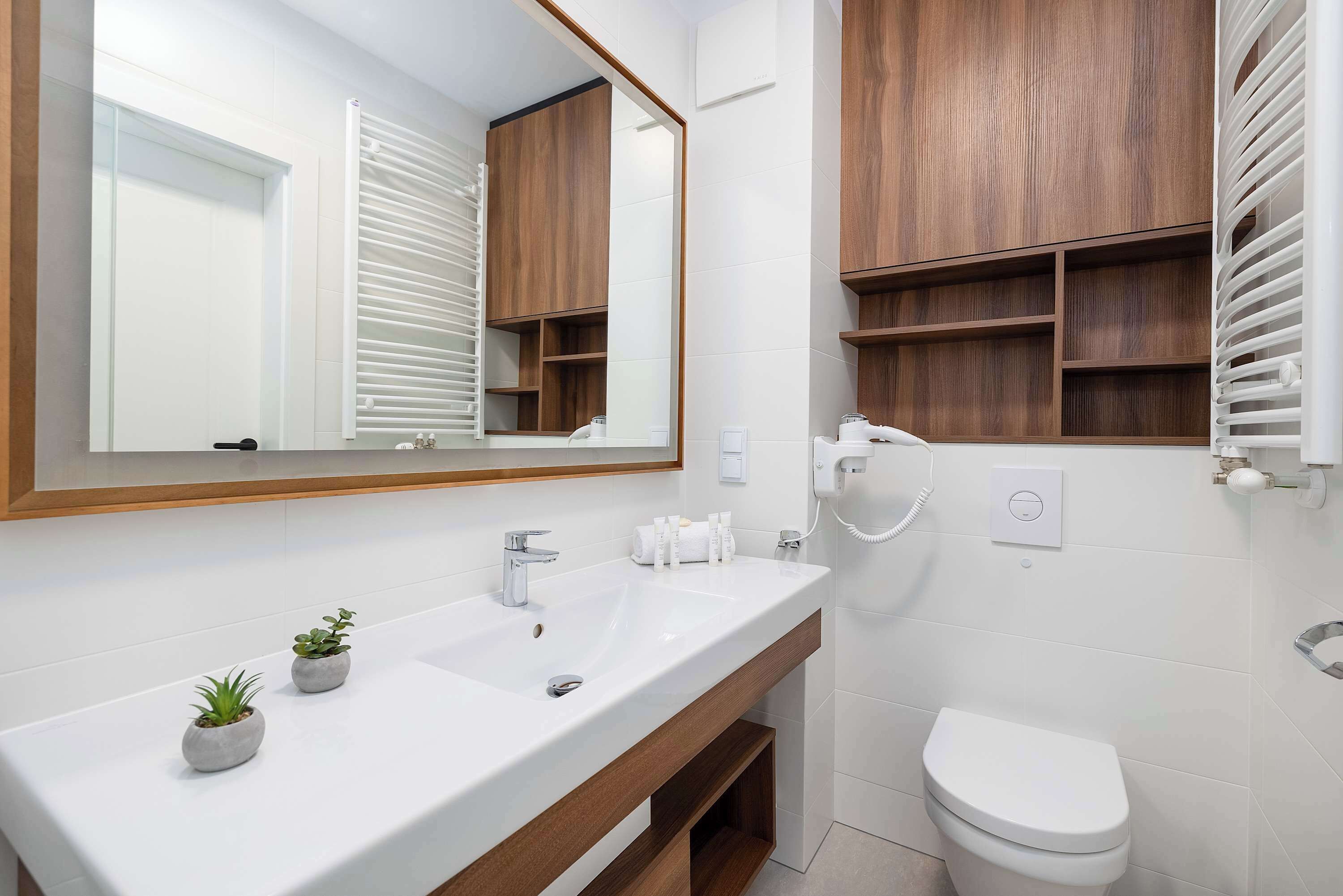 Un bagno moderno con un grande specchio, lavandino bianco, mobile contenitore in legno e un water.