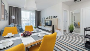 A modern hotel room with a dining area, a TV, and a balcony with curtains.