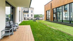 Une terrasse extérieure moderne, dotée d’une plateforme en bois, d’une pelouse verdoyante et offrant une vue sur les bâtiments adjacents.