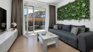 Een moderne woonkamer met een grijze bank, een bijzettafeltje, een televisie op een witte console, en een groene wanddecoratie.