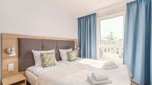 Ein Hotelzimmer mit einem großen Bett, einem Holzkopfende, einem Nachttisch, einer Lampe und einem Fenster mit Vorhängen.