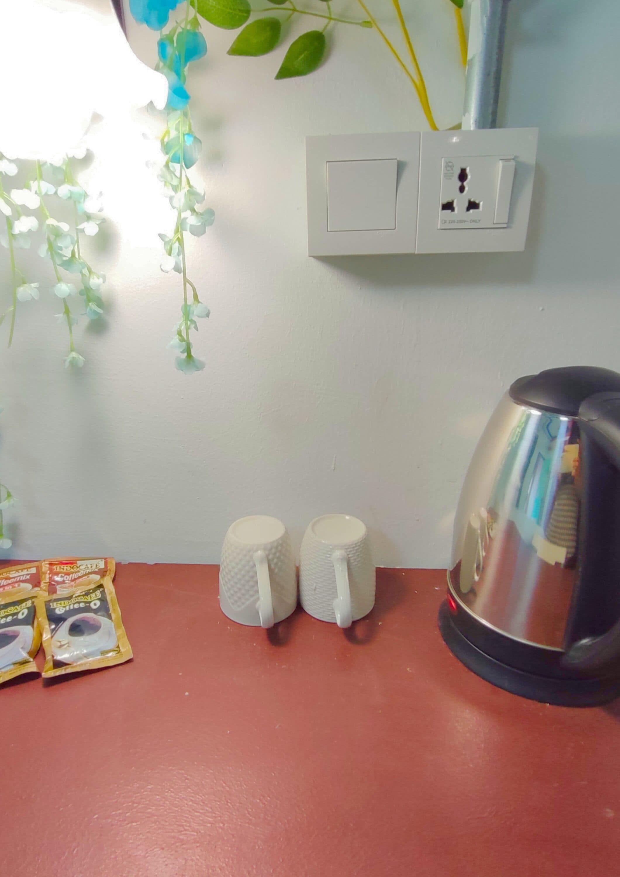 A kitchen counter with a kettle, two paper cups, and a packet of coffee pods.