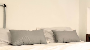 Ein ordentlich bezogenes Bett mit weißer Bettwäsche und zwei grauen Kissen.