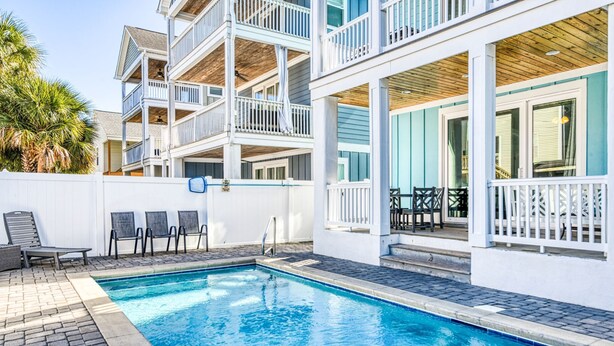 Un espace piscine doté d’une terrasse en bois, de rampes blanches et d’un coin salon avec des chaises.