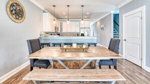 Un espace repas comprenant une grande table en bois, des chaises à revêtement noir et un îlot central doté d’un évier et d’appareils électroménagers.