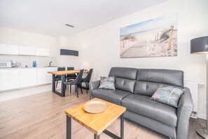 Uma sala de estar moderna com um sofá cinzento, mesa de centro de madeira e uma área de jantar com mesa e cadeiras de madeira.