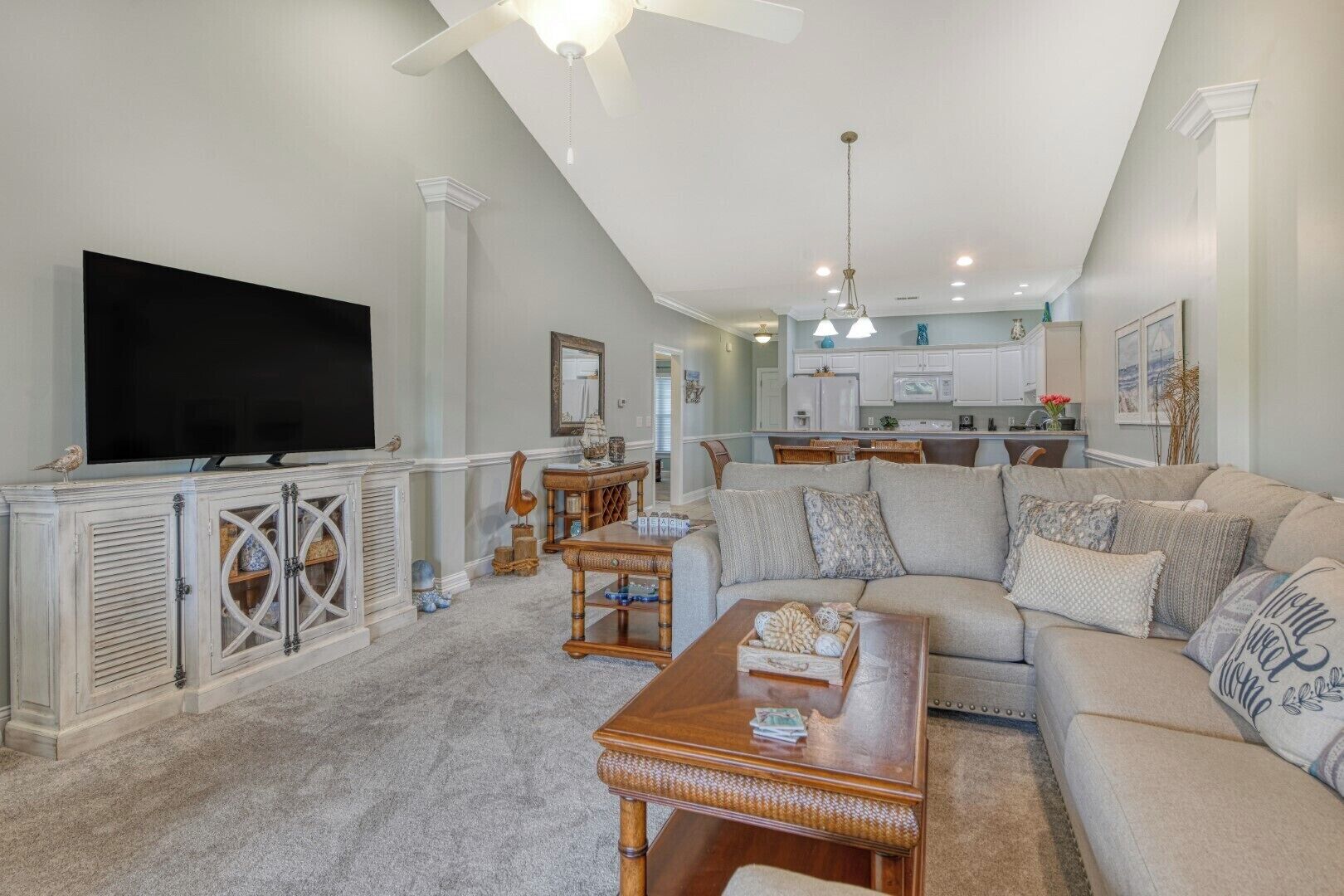 A spacious living room with a large sectional sofa, a wooden coffee table, and a flat-screen TV mounted on a white cabinet.