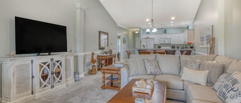A spacious living room with a large sectional sofa, a wooden coffee table, and a flat-screen TV mounted on a white cabinet.