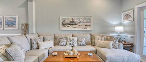 A living room with a sectional sofa, a wooden coffee table, and framed artwork on the walls.